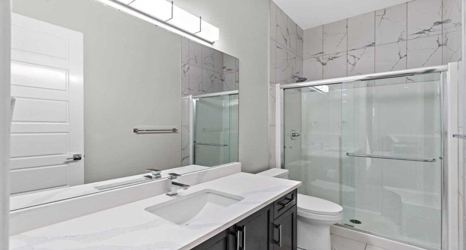 A beautifully appointed main floor 3 piece bath showcases sleek quartz countertops, a glass enclosed shower, and elegant tile detailing — offering both everyday practicality and refined convenience for guests and family alike.
