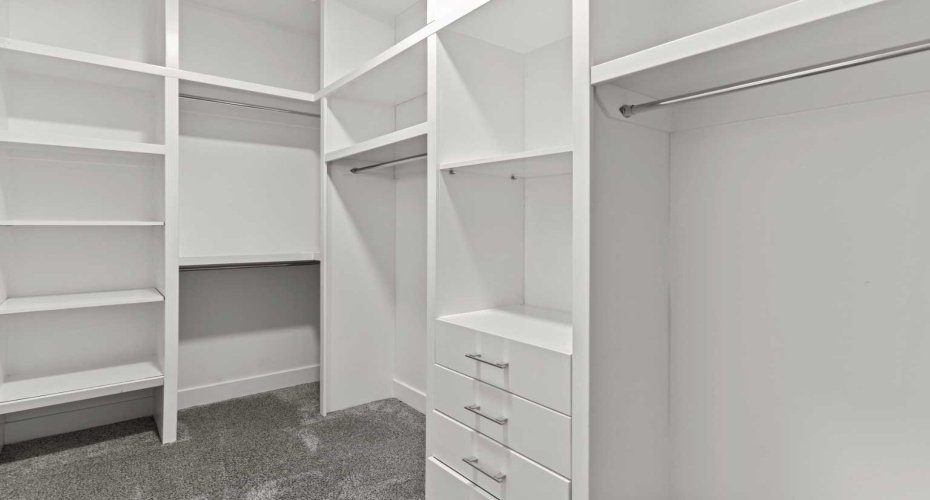 A custom built walk in closet with integrated shelving, drawers, and hanging space offers exceptional organization and boutique style storage within the primary suite.
