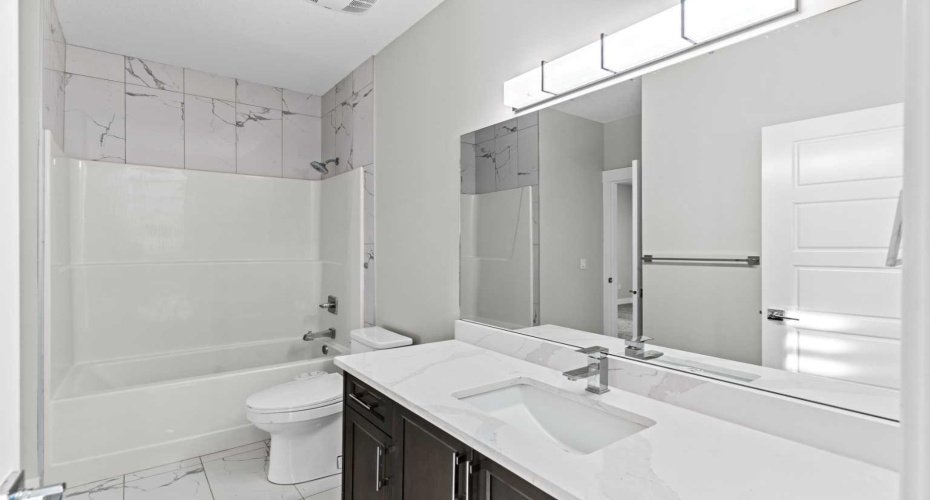 The third bedroom is complemented by a connected full bathroom featuring modern tile work, a sleek quartz vanity, and a tub shower combination for everyday comfort and convenience.