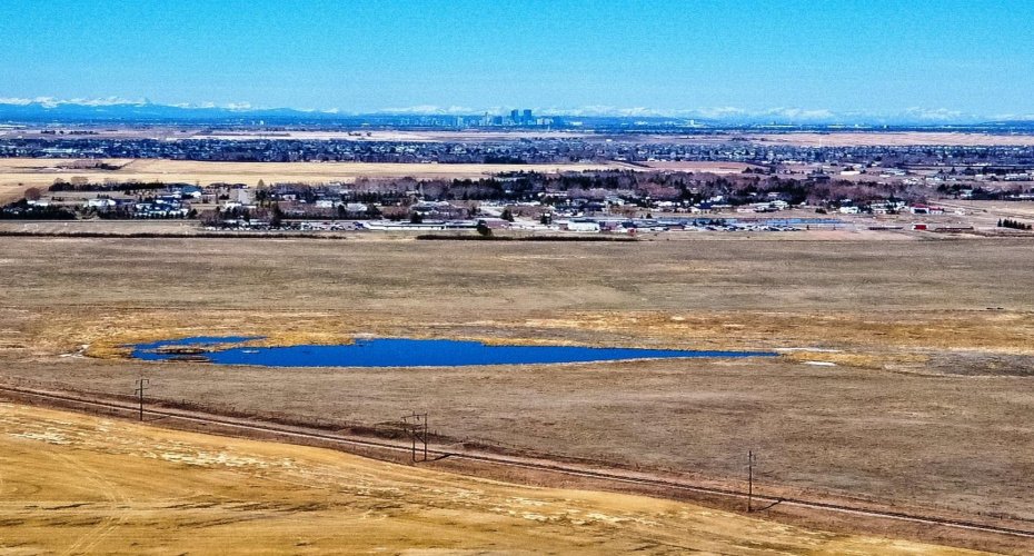 Drone view west. Chestermere High School in midground. Calgary and mountains beyond.