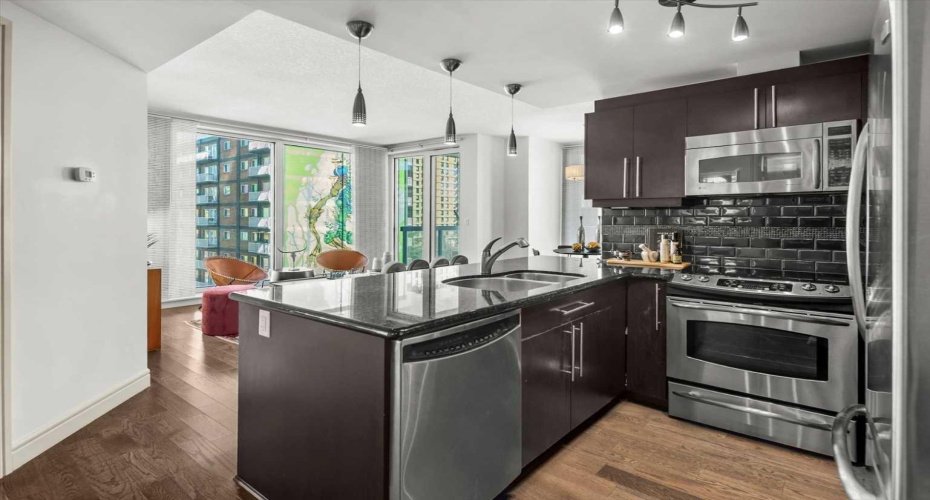 The kitchen is the heartbeat of this open floor plan and opens directly to the living room, where two walls of floor-to-ceiling windows bring the neighbourhood in. The large street mural visible from inside adds a personality to the view that no high-floor unit could replicate.