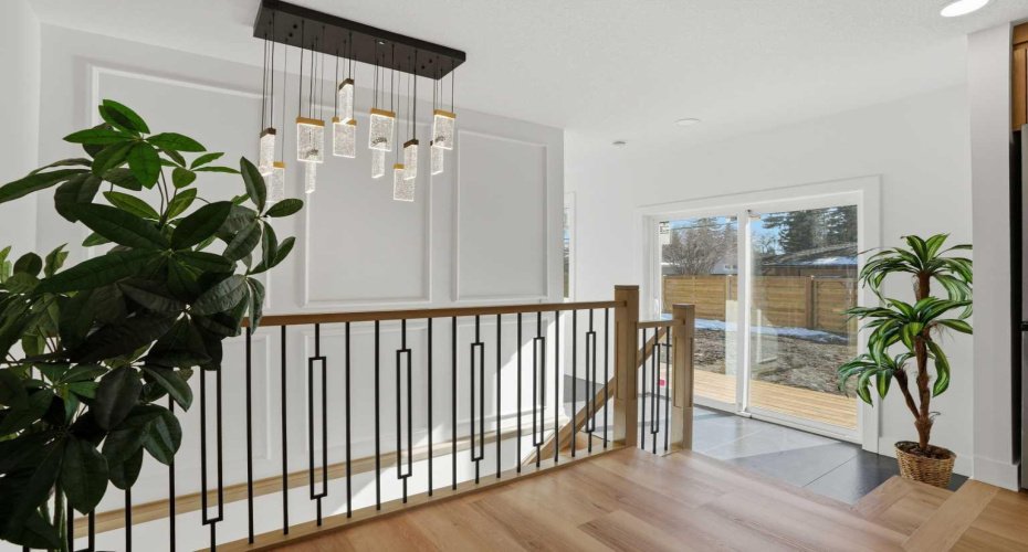 Sun-filled area with a beautiful feature wall, statement lighting, stylish railing, and sleek tile flooring, leading to patio doors that open onto the back deck and south-facing backyard.