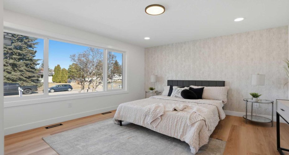 Spacious third bedroom featuring a large window that fills the room with natural light, complemented by a designer feature wall and modern finishes.