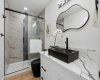 Modern washroom showcasing a fully tiled walk-in glass shower, quartz vanity with statement vessel sink, and upgraded black hardware for a clean, contemporary look.