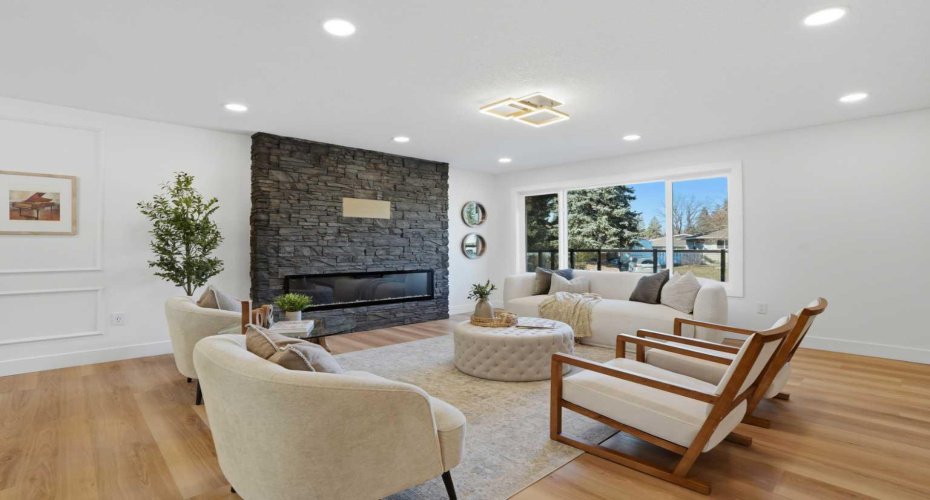 Modern living area with a sleek electric fireplace framed by floor-to-ceiling stonework, oversized window, and a massive front deck—perfect for indoor-outdoor living.