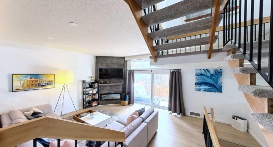 The spatial drop. Stepping down into the living room reveals ten-foot ceilings, a sleek dark-tiled gas fireplace, and those custom open-tread stairs.