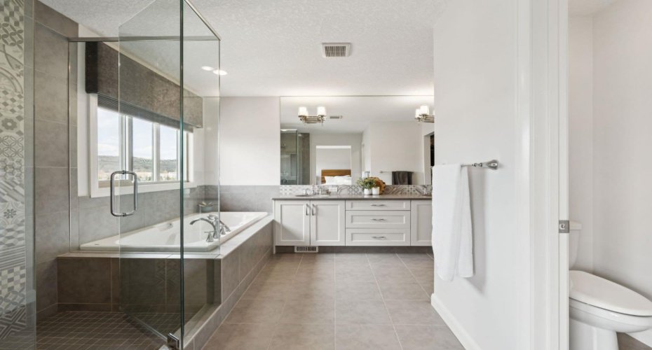 Spa-Inspired Primary Ensuite featuring a relaxing soaker tub, fully tiled shower, dual sinks, and a picture window  beautifully framing tree-lined river views