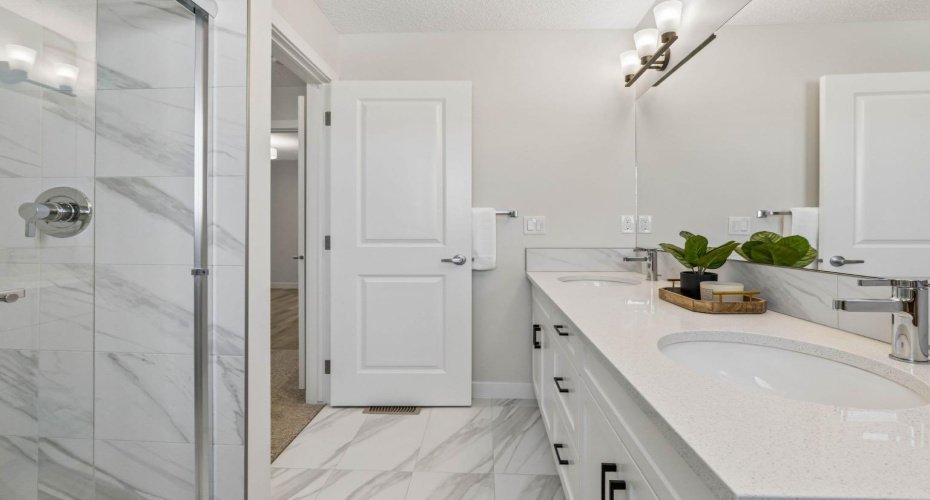 Designed for effortless mornings and relaxing evenings, this spa-inspired ensuite features dual vanities, quartz countertops, elegant marble-inspired tile, and a spacious glass shower.