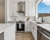 Designed with both style and function in mind, the kitchen showcases white shaker cabinetry, quartz countertops, a modern tile backsplash, stainless steel appliances, and a striking black farmhouse sink overlooking the backyard.