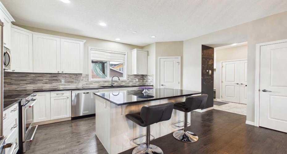 This view showcases the kitchen's stunning granite countertops, large island, corner pantry, abundant cabinetry, and open-concept layout, seamlessly connecting to the main-floor living and dining spaces.