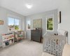 A bright second bedroom set up as a nursery, with two sunny windows and treed outlooks.