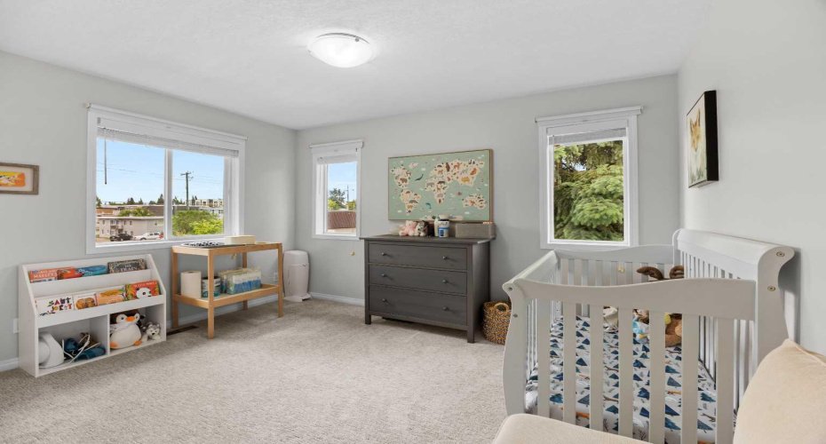 A bright second bedroom set up as a nursery, with two sunny windows and treed outlooks.