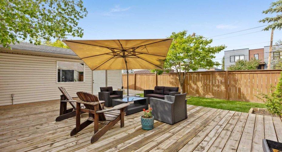 The sunny cedar deck steps down to a tidy fenced yard with a flowering tree and mature landscaping.