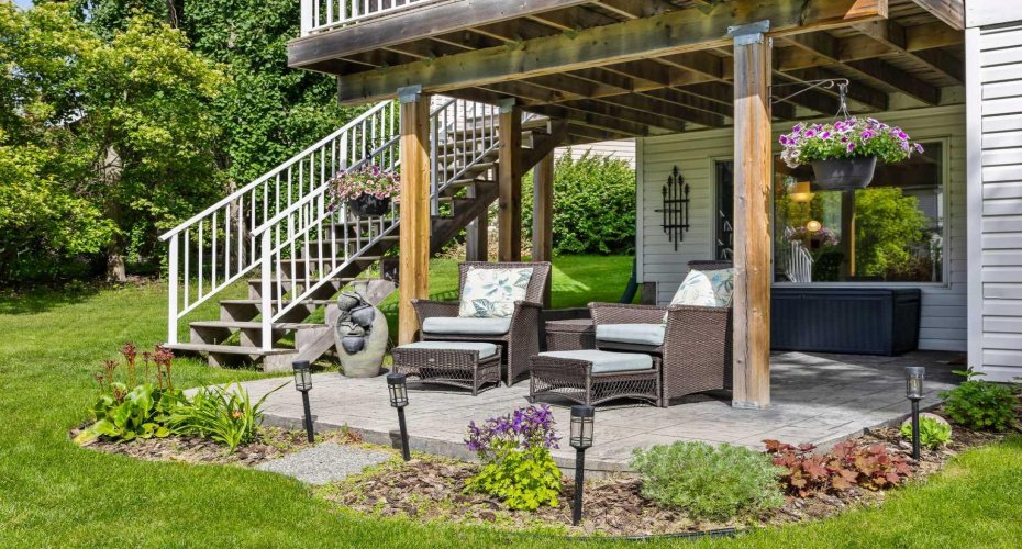 The walkout opens onto a covered stamped stone patio — shaded seating, garden views, and a quiet spot that works rain or shine.