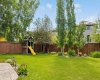 A kids' playhouse tucked to the side, mature trees for shade, and garden beds all around — this corner of the yard was made for childhood.