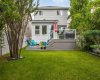 A full look at the back of the home: two storeys of bright windows, a tiered deck, and a generous lawn beyond. Space to garden, play, and gather, all wrapped in mature landscaping.