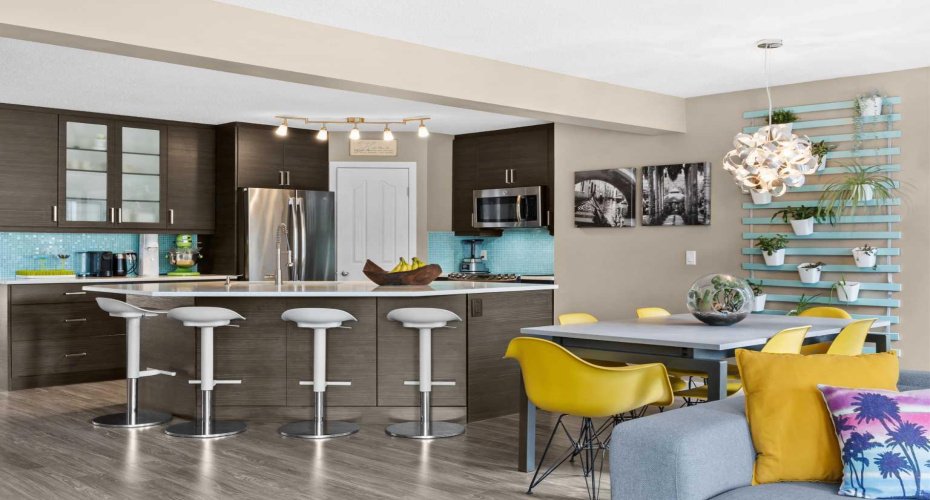 Kitchen, dining, and living move together as one bright, connected space. Pops of colour — the living plant wall, the sunny dining chairs — bring personality and life to the main floor.