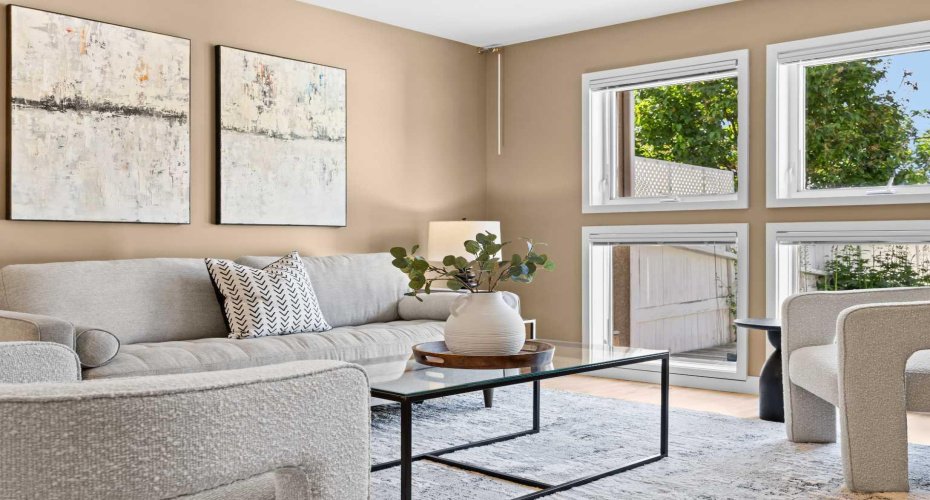 A bright, welcoming living space pairs comfortable seating with a wall of windows overlooking the yard.